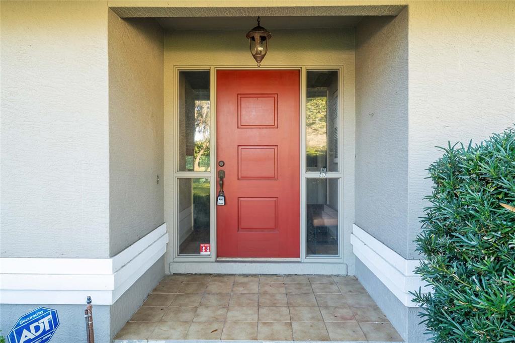 A red front door with side windows is set within a covered entryway — 8120 NW 48TH LANE, OCALA, FL
