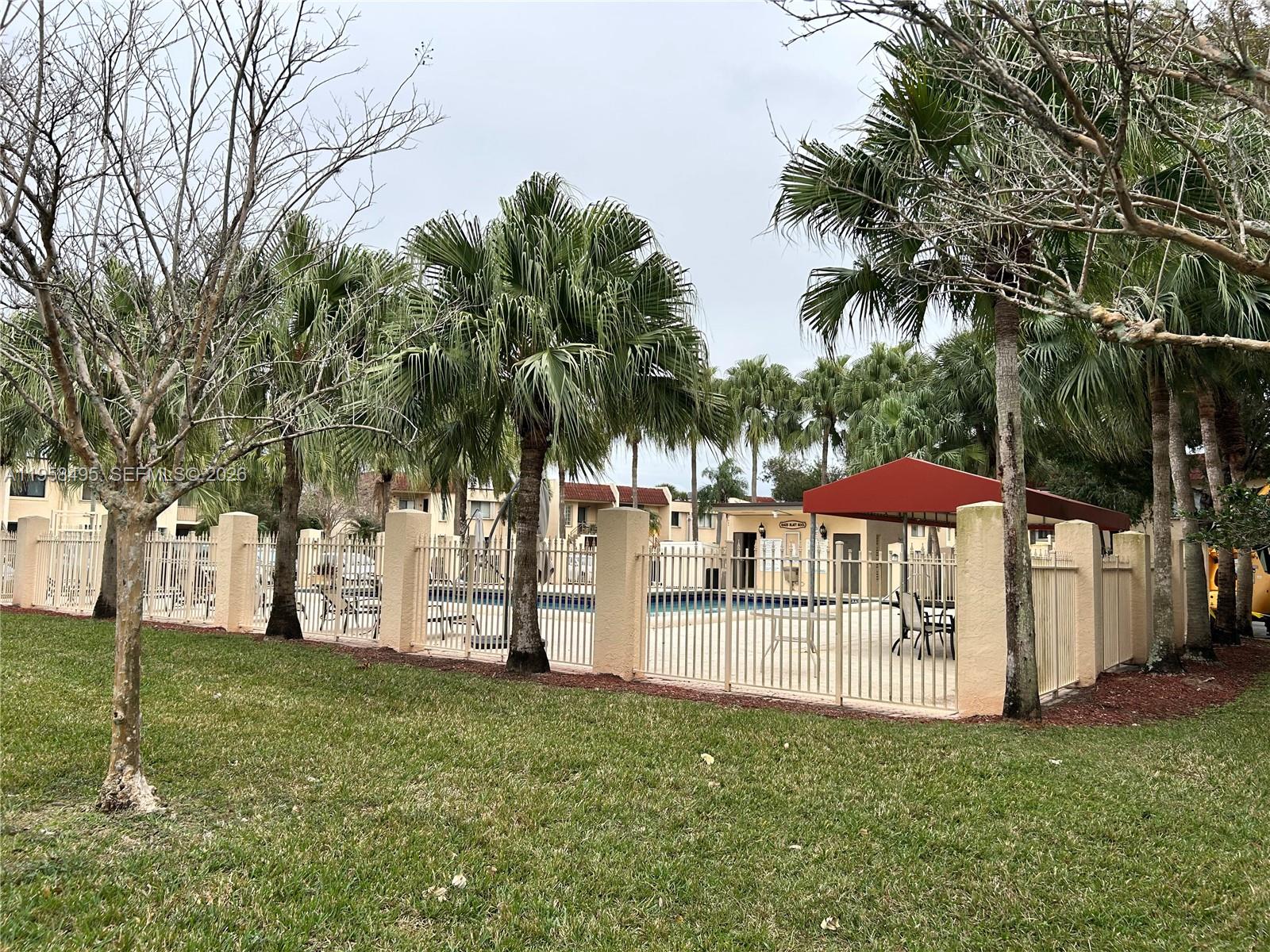 A fenced-in outdoor swimming pool area features palm trees, a red canopy, and lounge chairs — 16441 Blatt Blvd # 102, Weston FL 33326, WESTON, FL