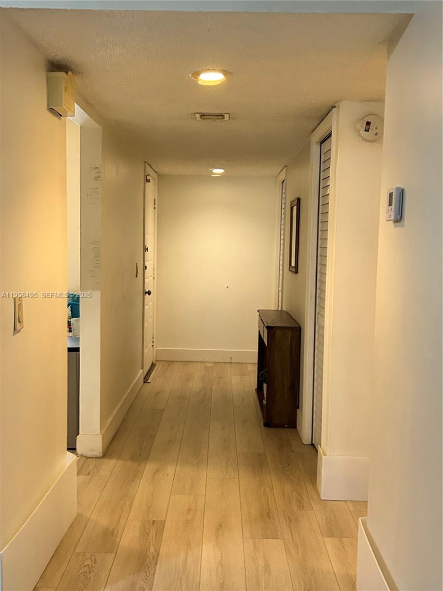 A hallway with light wood-look flooring leads to a white door and a wooden console — 16441 Blatt Blvd # 102, Weston FL 33326, WESTON, FL