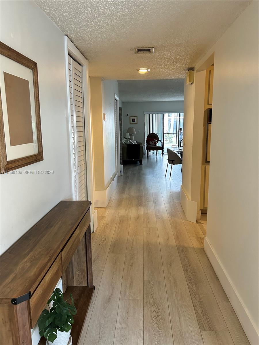A hallway with light wood-look flooring leads from a foyer toward a living area — 16441 Blatt Blvd # 102, Weston FL 33326, WESTON, FL