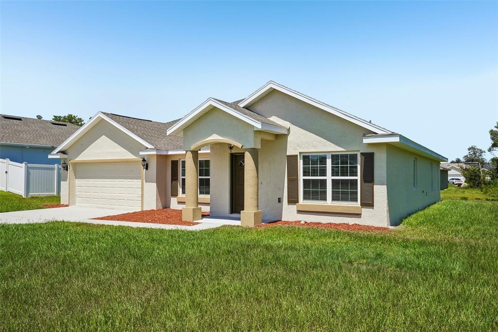 A single-story house with a beige stucco exterior, a two-car garage, and a covered entryway — 387 MARION OAKS LANE, OCALA, FL