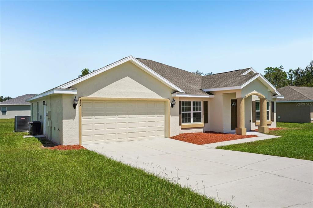 A single-story house with a beige stucco exterior, a two-car garage, and a covered entryway — 387 MARION OAKS LANE, OCALA, FL