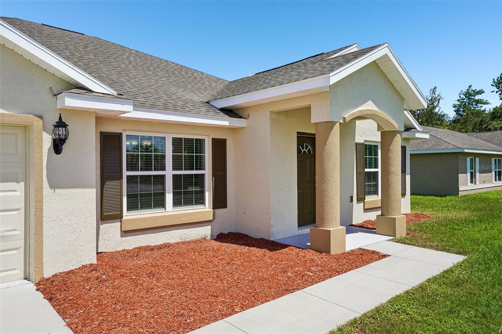 A single-story house exterior with a tan stucco facade, brown shutters, and a covered entryway — 387 MARION OAKS LANE, OCALA, FL