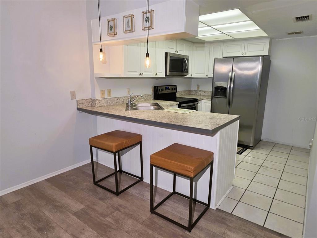 A kitchen features white cabinets, stainless steel appliances, a breakfast bar, and two leather stools — 1781 SAMURAI POINT UNIT P9, LUTZ, FL
