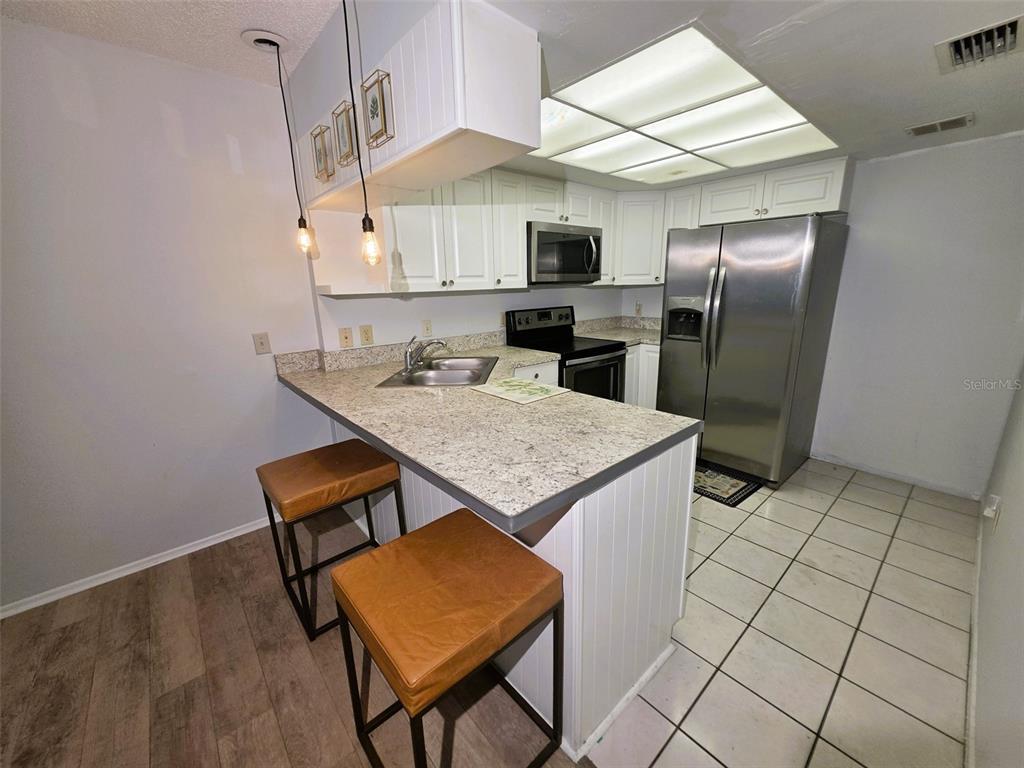 A kitchen features white cabinets, stainless steel appliances, a granite countertop, and two bar stools — 1781 SAMURAI POINT UNIT P9, LUTZ, FL