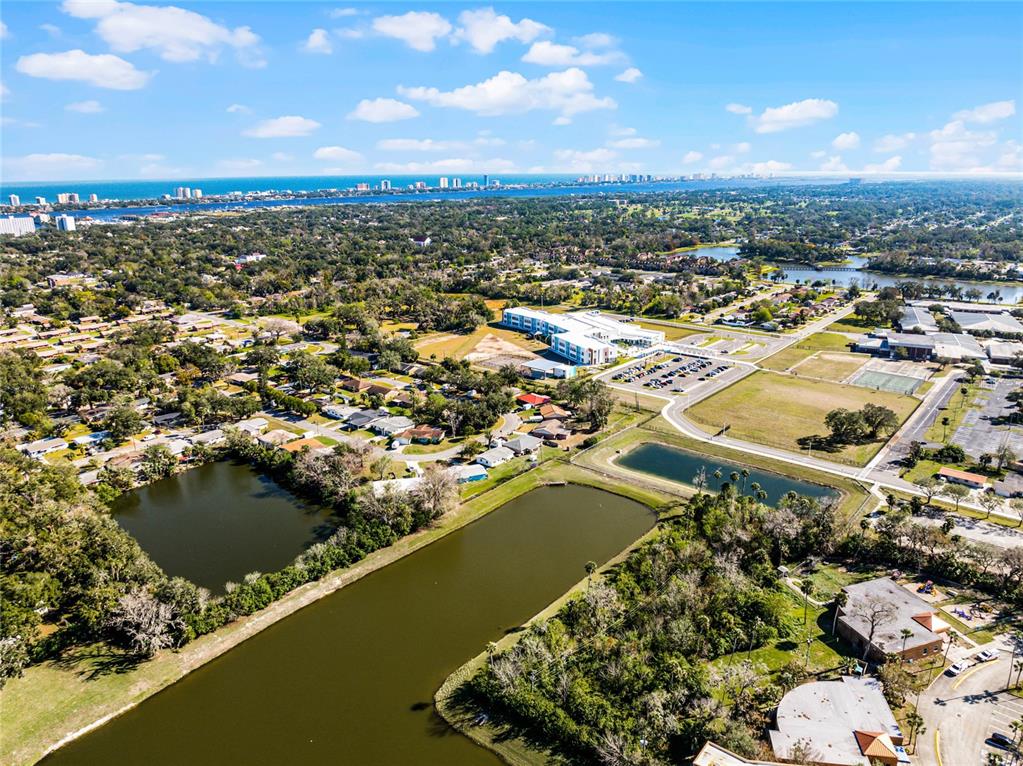 An aerial view shows a suburban landscape with ponds, residential homes, and a large building — 825 KOTTLE CIRCLE S, DAYTONA BEACH, FL