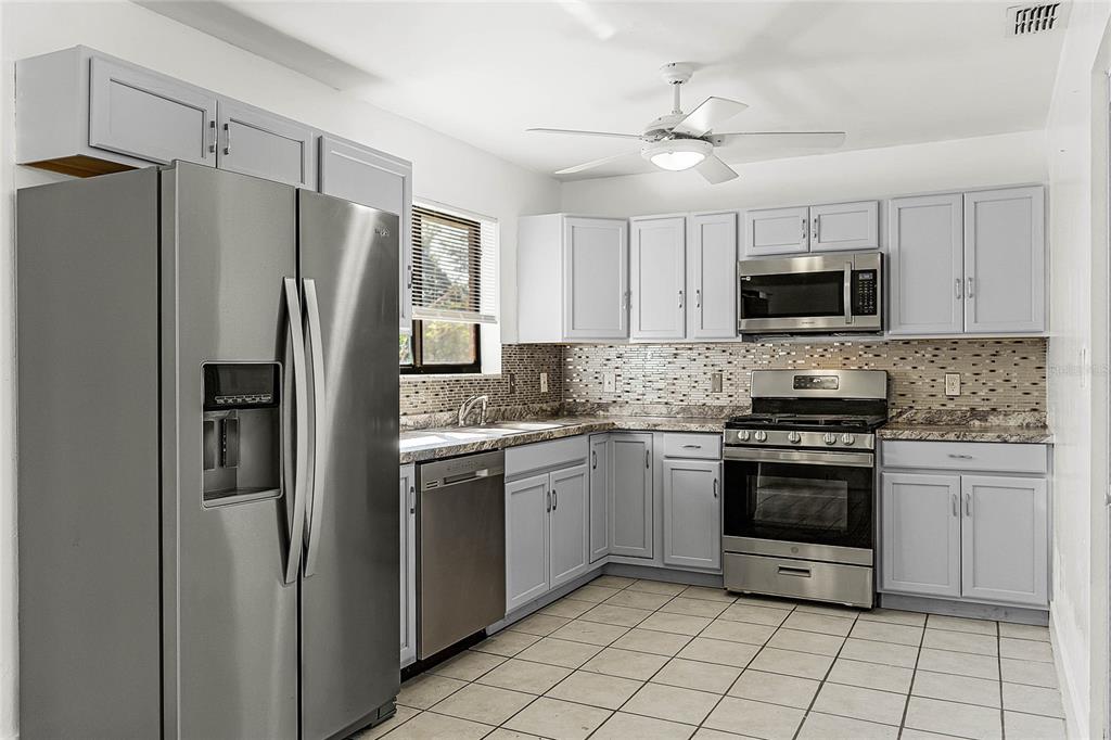 A kitchen features light gray cabinets, stainless steel appliances, a tiled backsplash, and tile flooring — 825 KOTTLE CIRCLE S, DAYTONA BEACH, FL