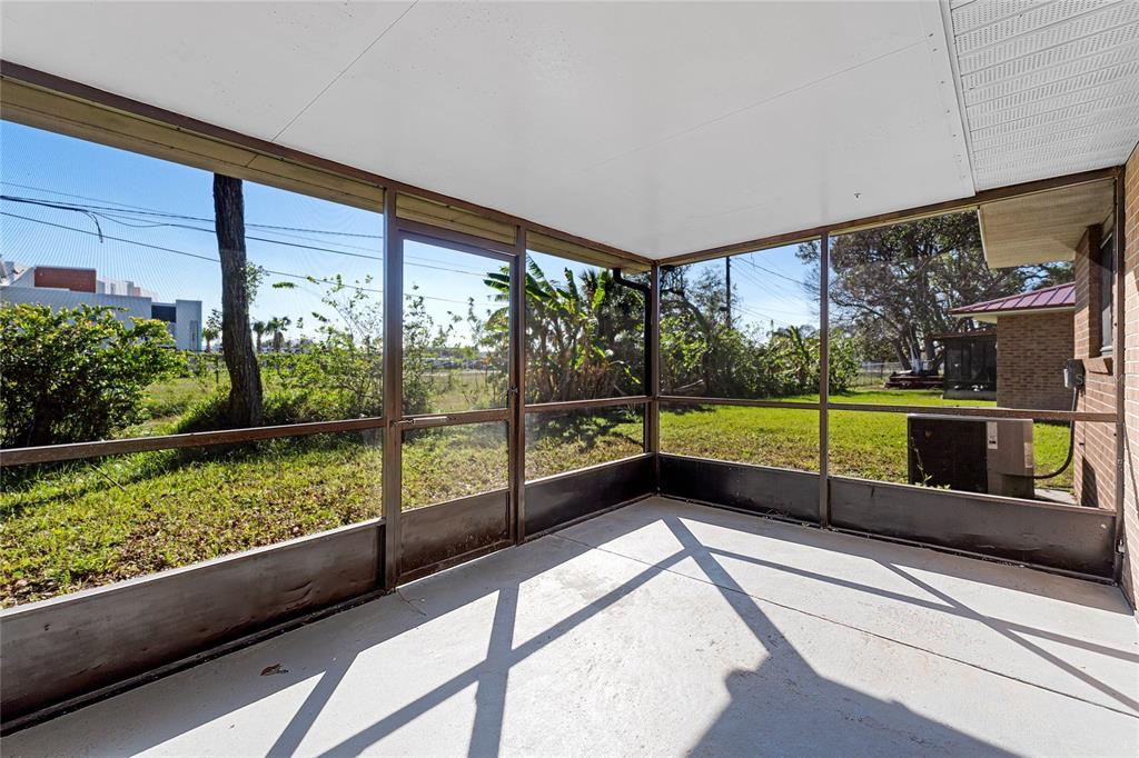 A screened-in porch with a concrete floor overlooks a grassy backyard with trees — 825 KOTTLE CIRCLE S, DAYTONA BEACH, FL