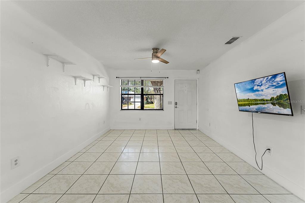 A living room features white walls, tile flooring, a ceiling fan, and a wall-mounted television — 825 KOTTLE CIRCLE S, DAYTONA BEACH, FL