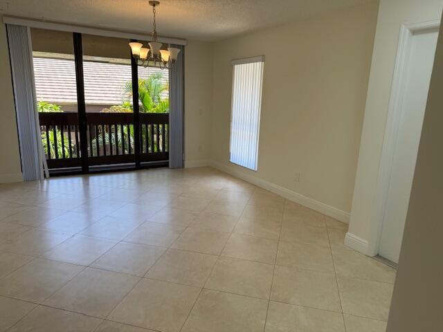 An empty room with light-colored tile flooring, a chandelier, and a sliding glass door balcony — 9256 Sabal Ridge Circle # D, Boca Raton FL 33428, BOCA RATON, FL