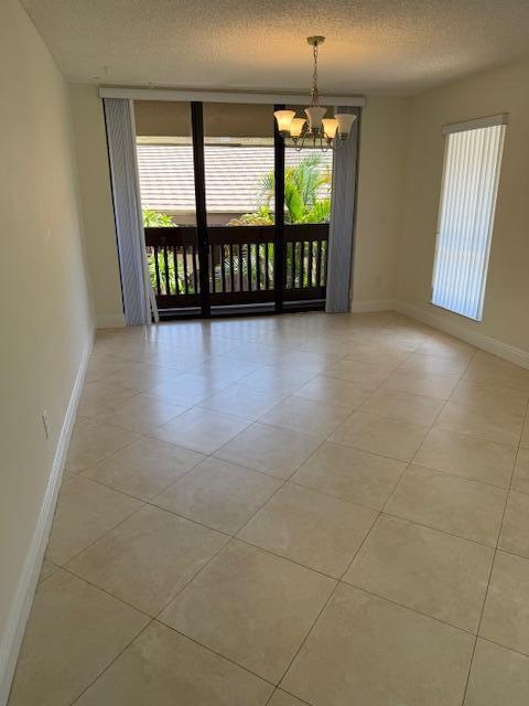 An empty dining room with beige tile floors, a chandelier, and sliding glass balcony doors — 9256 Sabal Ridge Circle # D, Boca Raton FL 33428, BOCA RATON, FL