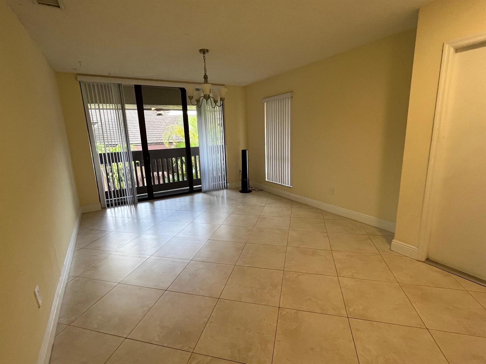 An empty dining room with beige tile floors, a chandelier, and a sliding glass door — 9256 Sabal Ridge Circle # D, Boca Raton FL 33428, BOCA RATON, FL