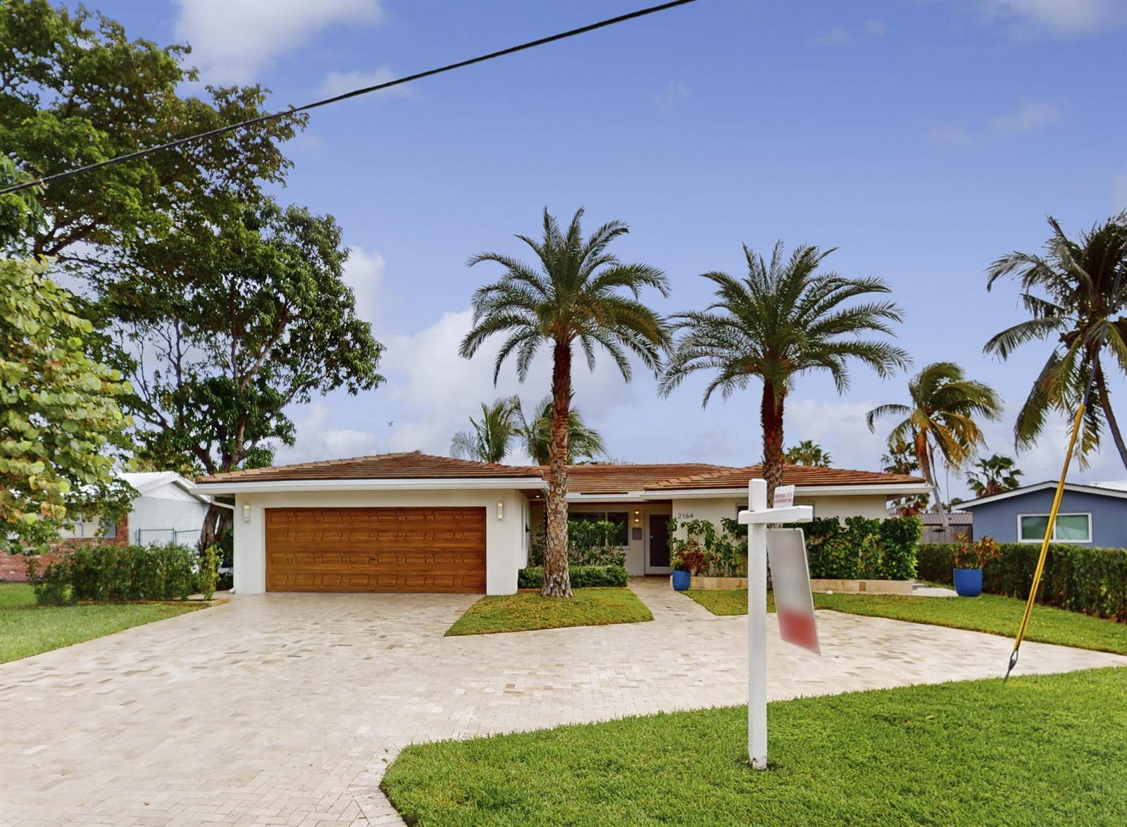 A single-story house with a paved driveway, two palm trees, and a for-sale sign — 2164 NE 25th Street, Wilton Manors FL 33305, WILTON MANORS, FL