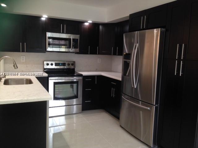 A modern kitchen features dark wood cabinets, stainless steel appliances, and light-colored countertops — 451 NE 210th Cir Ter # 19, Miami FL 33179, MIAMI, FL