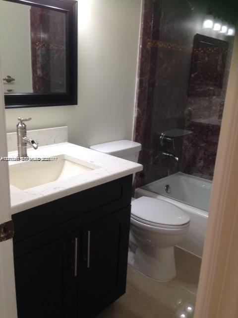 A bathroom features a dark vanity with a white countertop, a mirror, and a bathtub — 451 NE 210th Cir Ter # 19, Miami FL 33179, MIAMI, FL