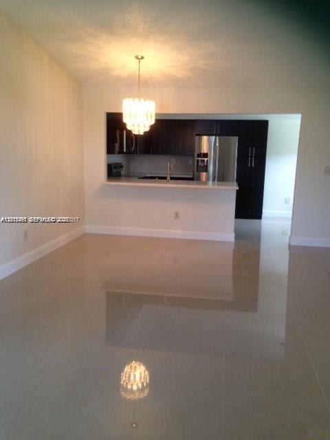 A dining area with a chandelier opens to a kitchen featuring dark cabinets and appliances — 451 NE 210th Cir Ter # 19, Miami FL 33179, MIAMI, FL