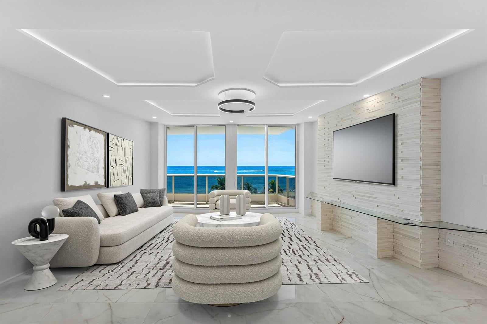A modern living room features a white sofa, circular ottoman, and ocean views through glass doors — 700 S Ocean Boulevard # 504, Boca Raton FL 33432, BOCA RATON, FL