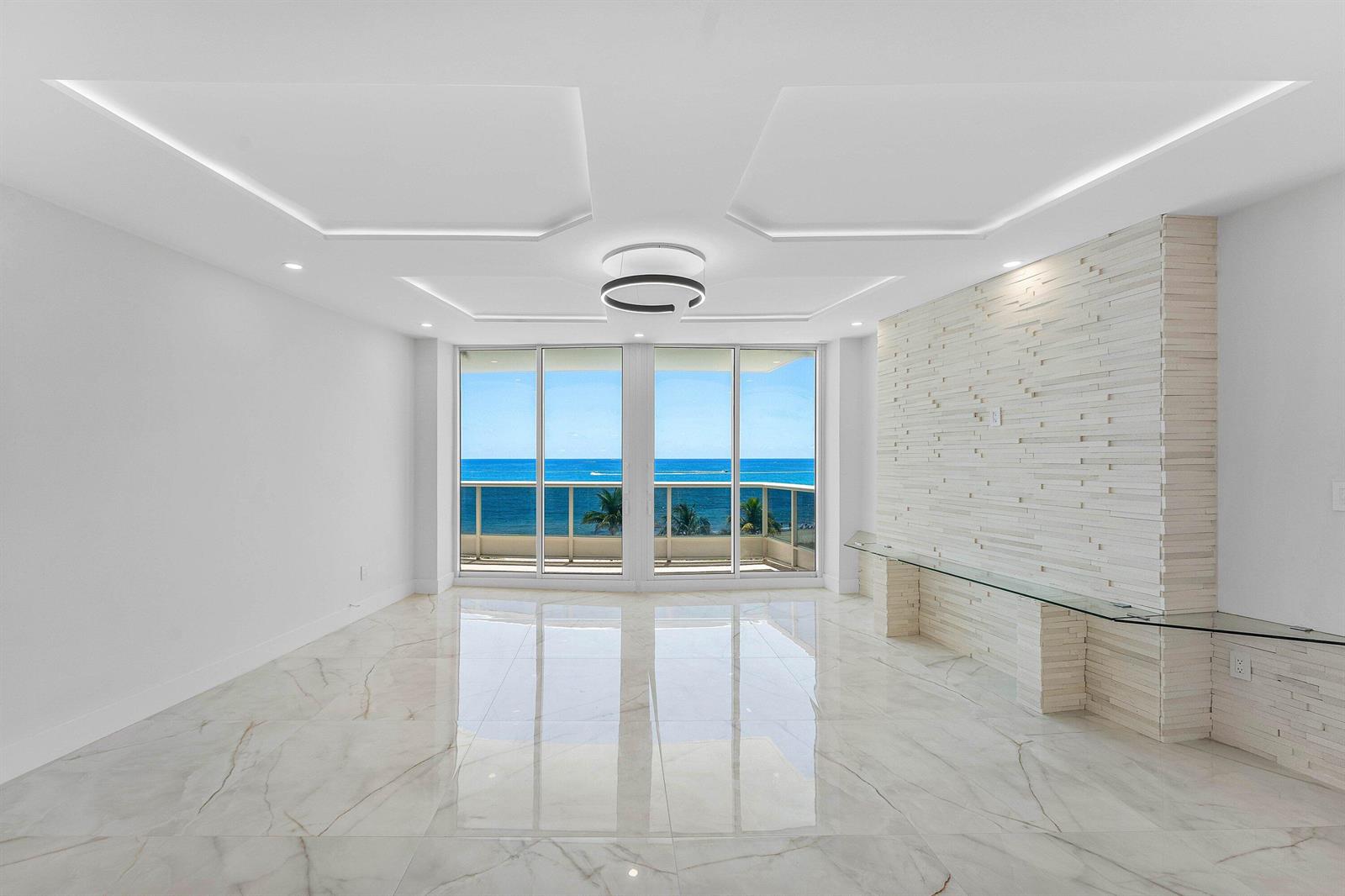 A bright living room features white marble floors, a textured stone wall, and ocean views — 700 S Ocean Boulevard # 504, Boca Raton FL 33432, BOCA RATON, FL