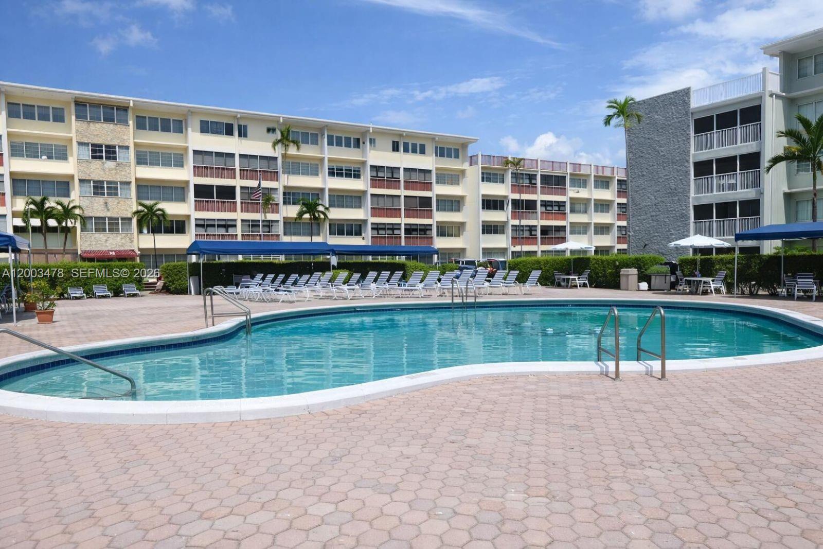 A swimming pool sits in front of a multi-story apartment building with a paved deck — 215 SE 3rd Ave # 306C, Hallandale Beach FL 33009, HALLANDALE BEACH, FL