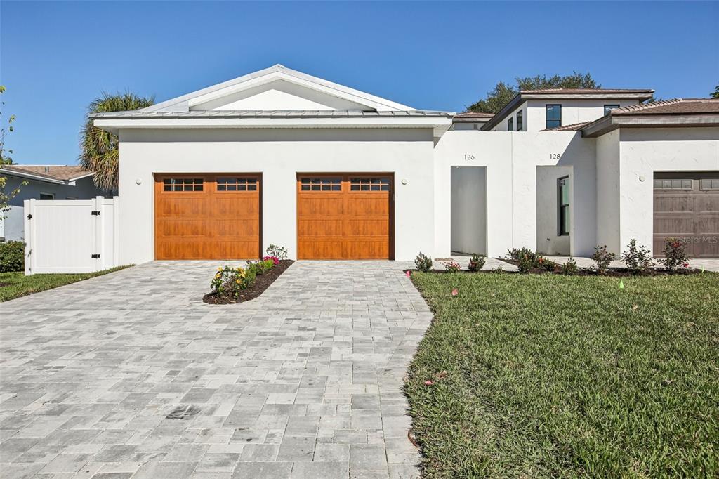 A white house exterior features two wooden garage doors and a paved driveway — 126 RICARDO WAY NE, ST PETERSBURG, FL