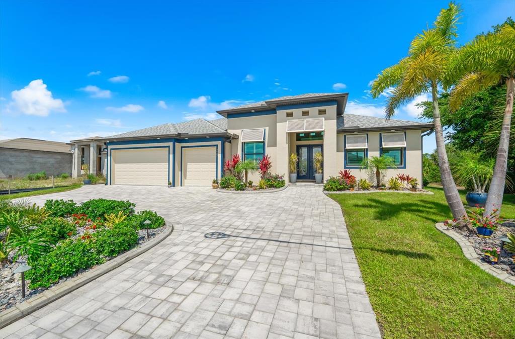 A single-story house with a paved driveway, two-car garage, and tropical landscaping under a blue sky — 13407 CHENILLE DRIVE, PORT CHARLOTTE, FL