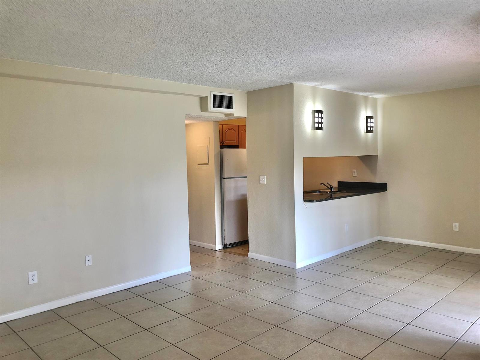 An open living area with tile flooring leads to a kitchen with a breakfast bar — 6031 10th Avenue N # 120, FL 33463, FL