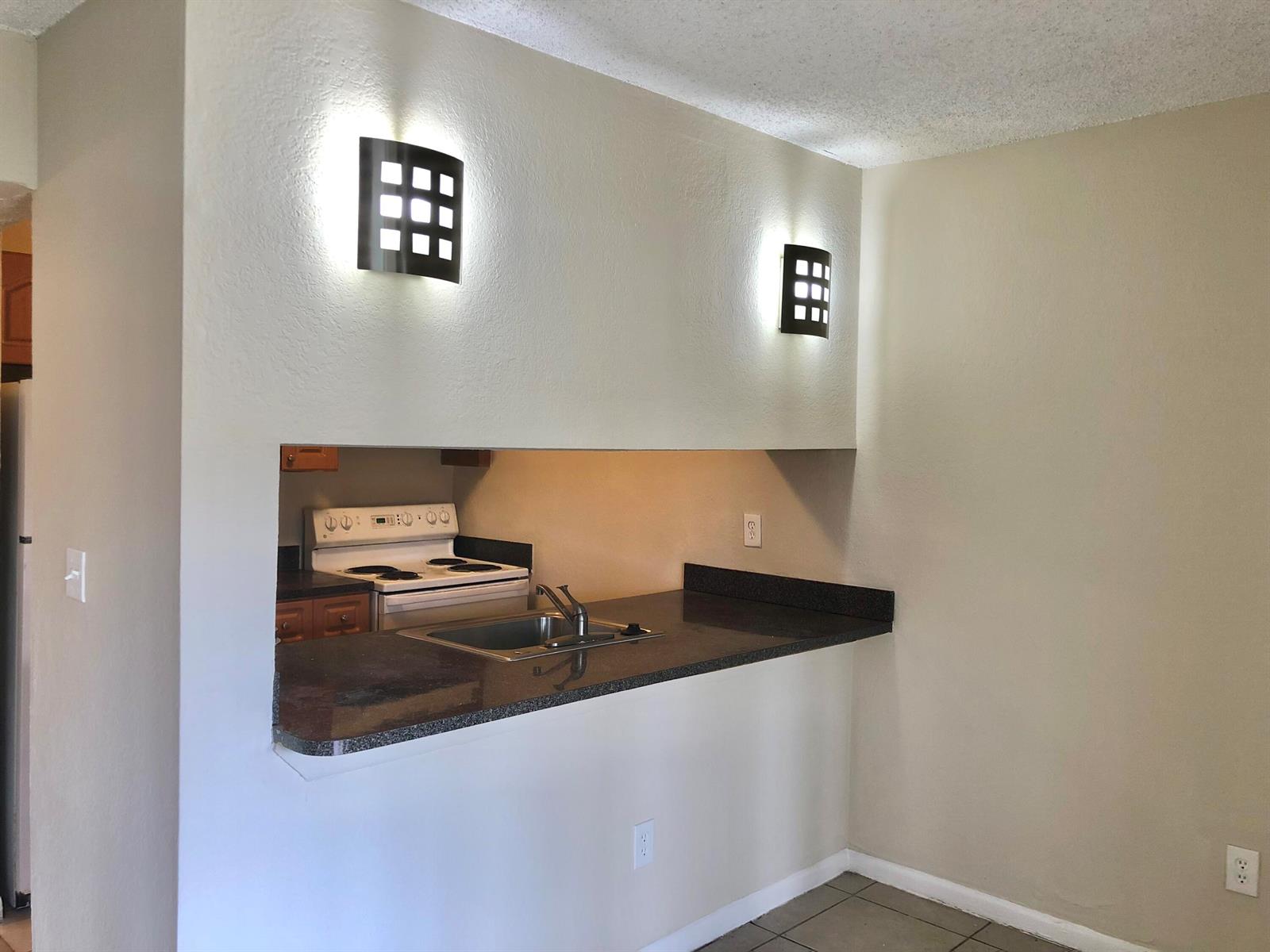 A kitchen pass-through window with a dark countertop and two wall-mounted light fixtures — 6031 10th Avenue N # 120, FL 33463, FL