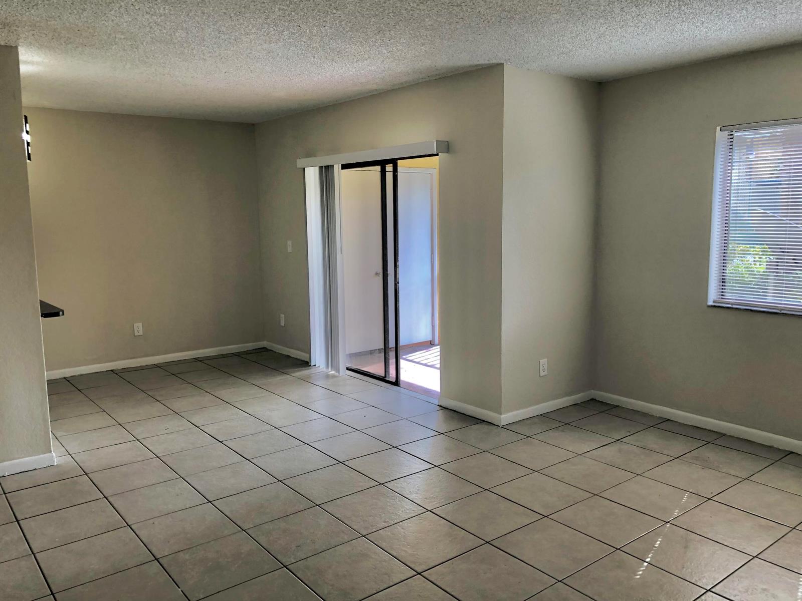 An empty living room with light-colored tile flooring, beige walls, and a sliding glass door — 6031 10th Avenue N # 120, FL 33463, FL