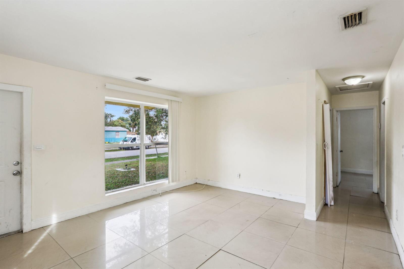 An empty room with light-colored tile flooring, a large window, and a hallway entrance — 520 NE 45th Street, Deerfield Beach FL 33064, DEERFIELD BEACH, FL