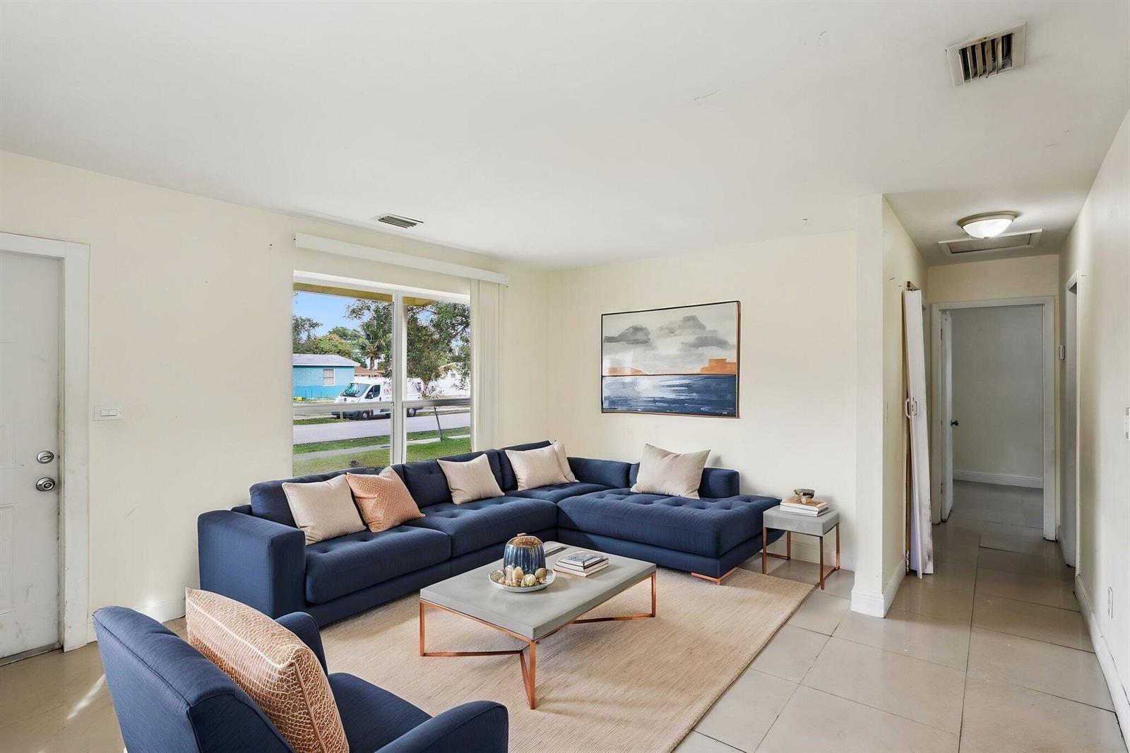 A living room features a blue sectional sofa, a coffee table, and a large window — 520 NE 45th Street, Deerfield Beach FL 33064, DEERFIELD BEACH, FL