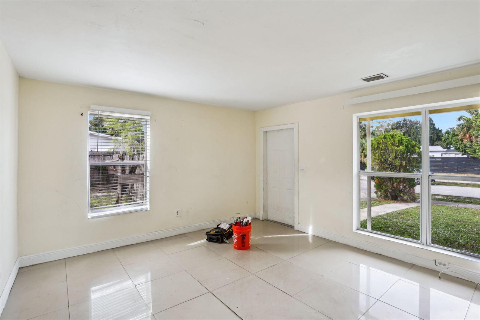 An empty room features light-colored tile flooring, cream walls, two windows, and a white door — 520 NE 45th Street, Deerfield Beach FL 33064, DEERFIELD BEACH, FL