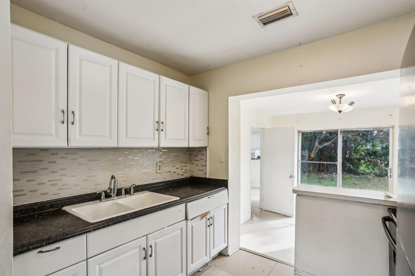 A kitchen with white cabinets, a dark countertop, a white sink, and a tiled backsplash — 520 NE 45th Street, Deerfield Beach FL 33064, DEERFIELD BEACH, FL