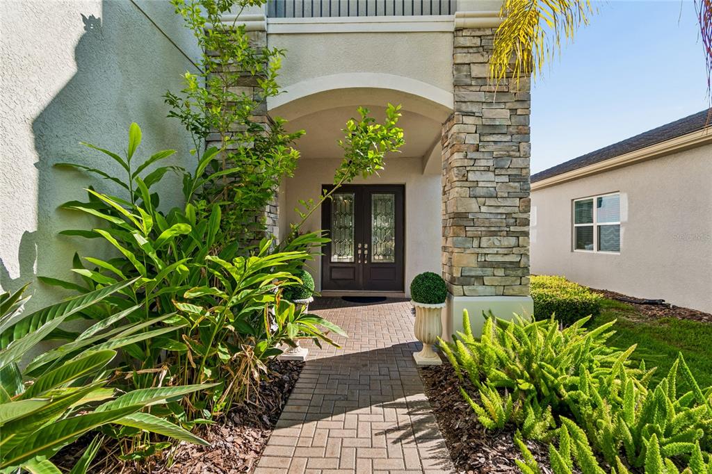 A paved walkway leads to a covered entryway with double doors and stone pillar accents — 30229 SOUTHERNWOOD COURT, WESLEY CHAPEL, FL
