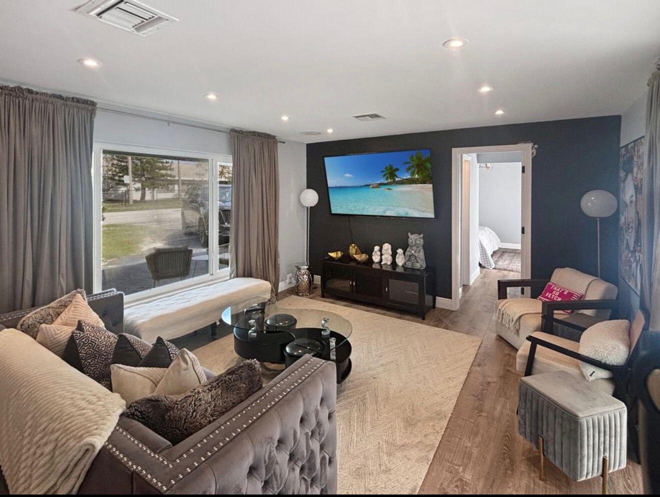 A living room features a dark accent wall with a mounted television and wood flooring — 100 SW 17th Street, Pompano Beach FL 33060, POMPANO BEACH, FL