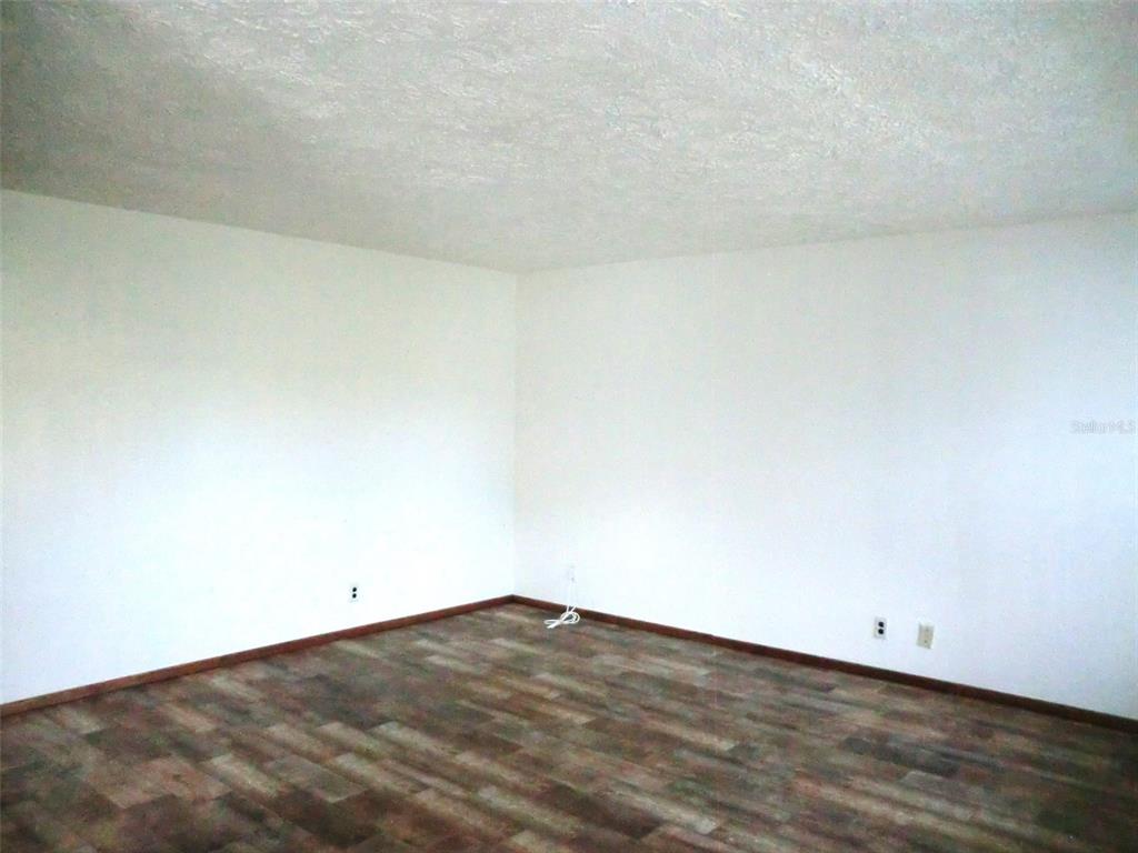 An empty room features white walls, wood-look flooring, and a textured ceiling — 202 BEDFORD TRAIL UNIT 112, SUN CITY CENTER, FL