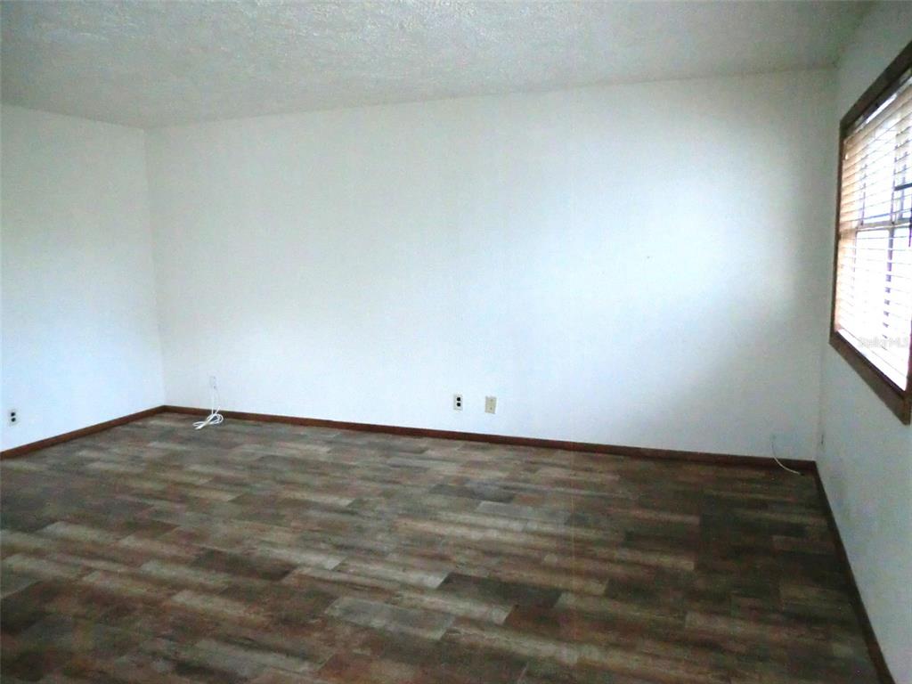 An empty room with white walls, wood-look flooring, and a window with blinds — 202 BEDFORD TRAIL UNIT 112, SUN CITY CENTER, FL