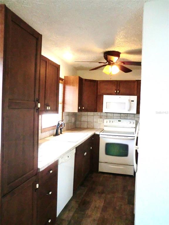 A kitchen features dark wood cabinets, white appliances, tiled countertops, and wood-look flooring — 202 BEDFORD TRAIL UNIT 112, SUN CITY CENTER, FL