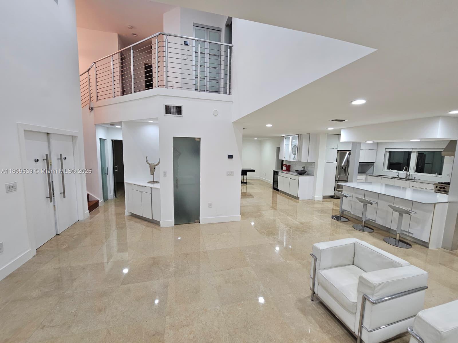 A modern, open-concept living area features a white kitchen, marble floors, and a mezzanine balcony — 5754 NW 98th Ave, Doral FL 33178, DORAL, FL