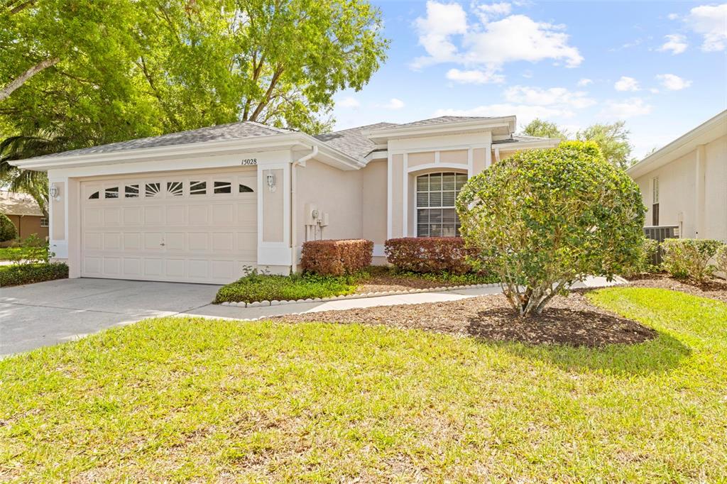 A single-story house with a beige stucco exterior, a two-car garage, and a front lawn — 15028 MIDDLE FAIRWAY DRIVE, SPRING HILL, FL