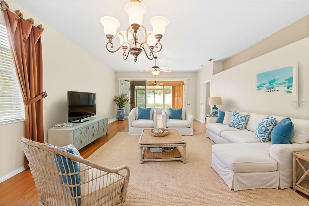A living room features a chandelier, white sofas, a wicker coffee table, and hardwood floors — 15028 MIDDLE FAIRWAY DRIVE, SPRING HILL, FL