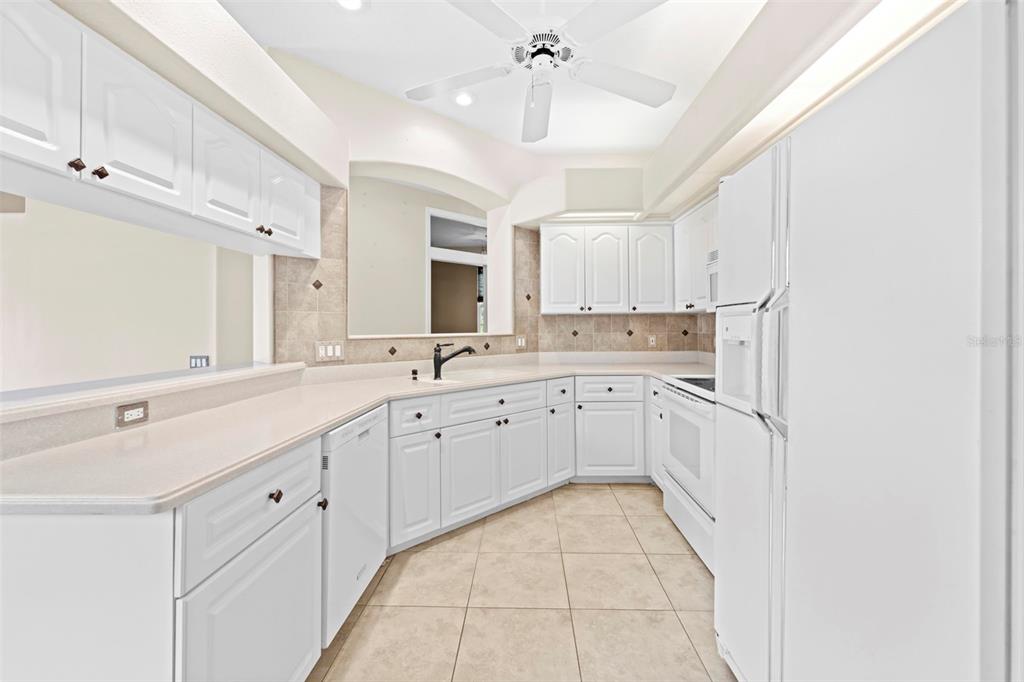 A kitchen features white cabinetry, light countertops, tile flooring, and a ceiling fan — 15028 MIDDLE FAIRWAY DRIVE, SPRING HILL, FL
