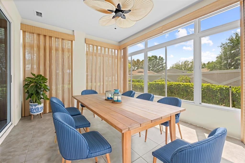 A sunroom features a wooden dining table, blue chairs, and large windows overlooking a hedge — 15028 MIDDLE FAIRWAY DRIVE, SPRING HILL, FL