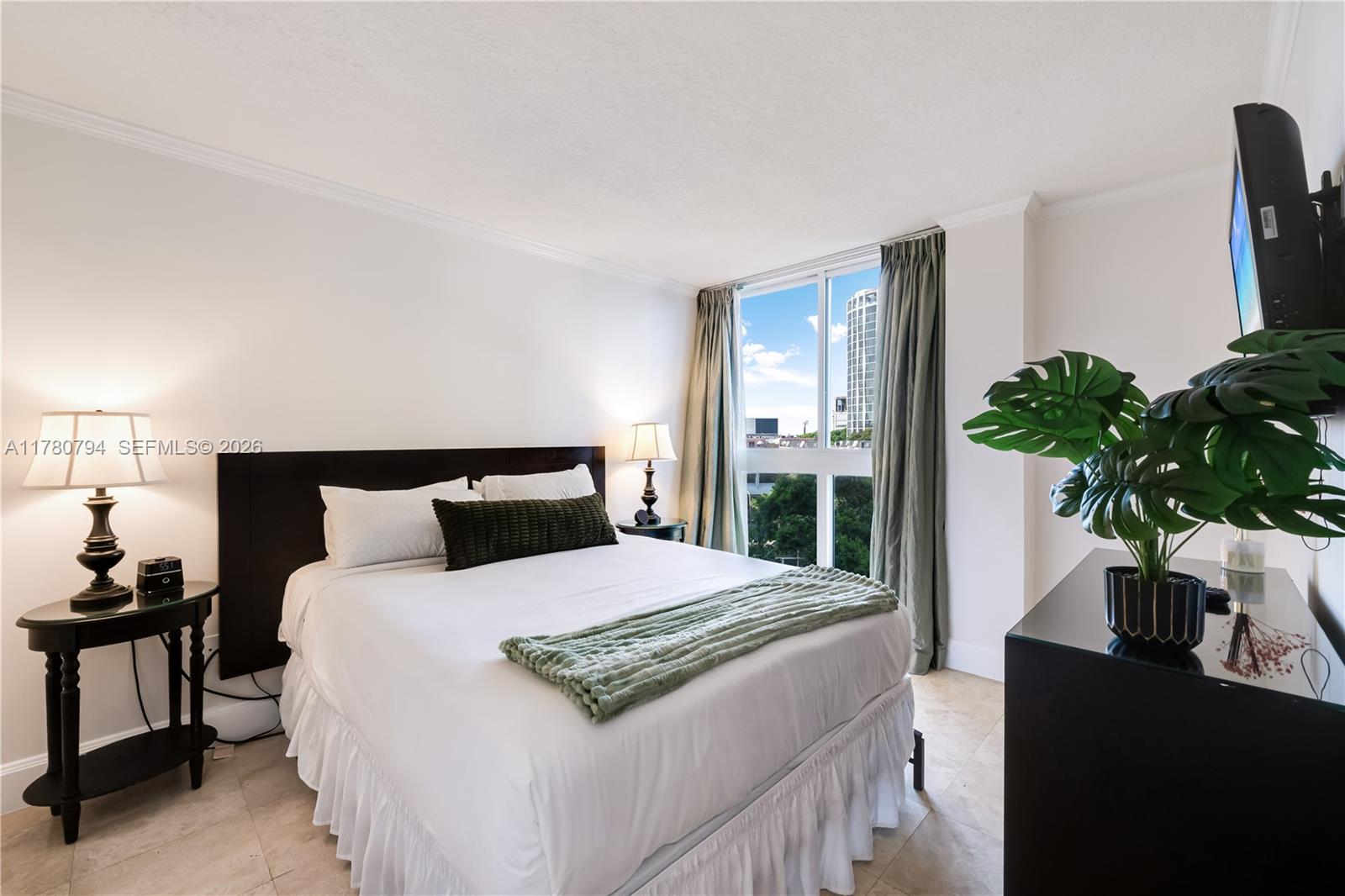 A bedroom features a bed with a white ruffled skirt, dark furniture, and a window view — 2951 S Bayshore Dr # 815, Miami FL 33133, MIAMI, FL
