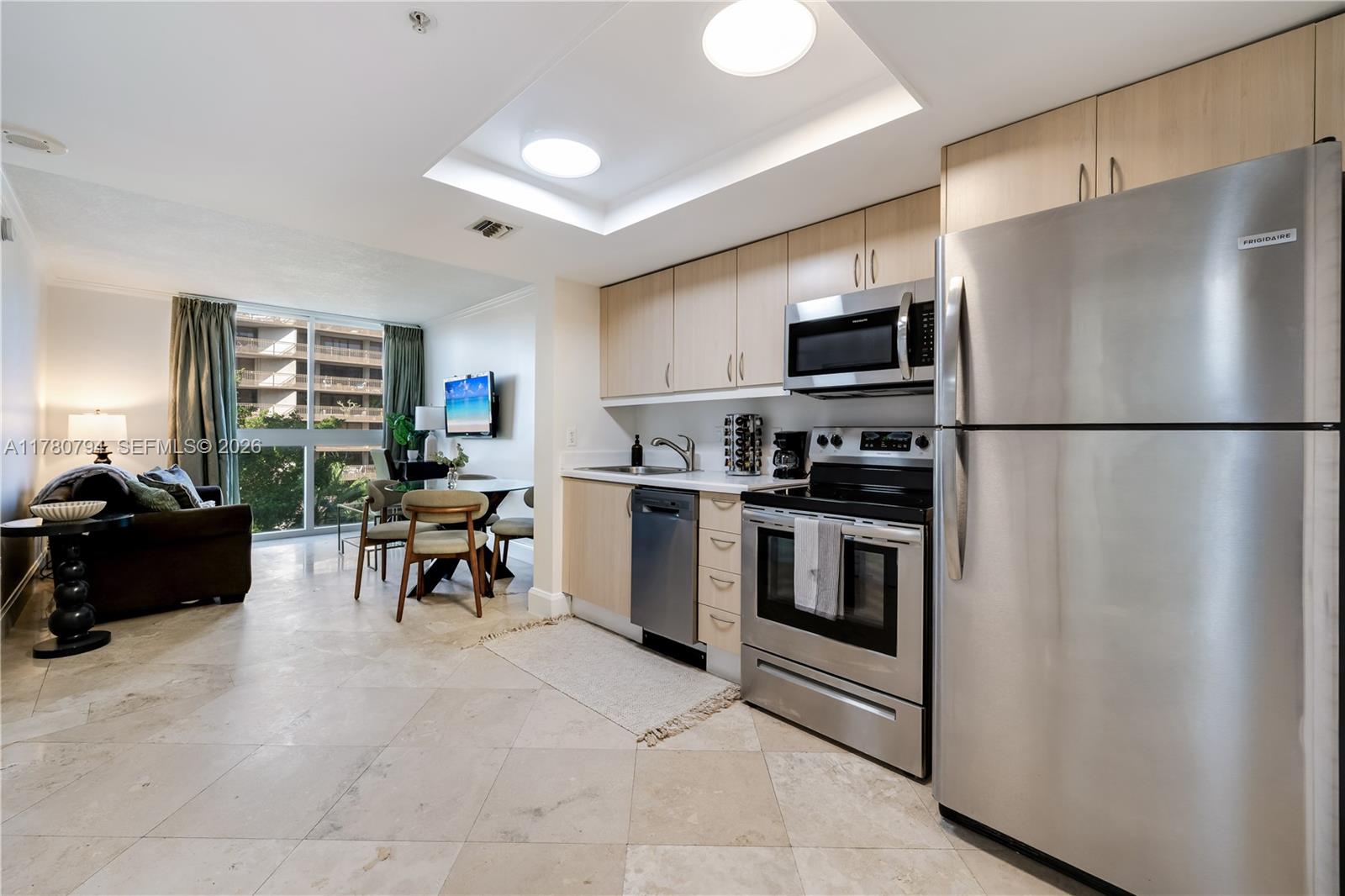 A kitchen with stainless steel appliances and light wood cabinets opens into a living area — 2951 S Bayshore Dr # 815, Miami FL 33133, MIAMI, FL