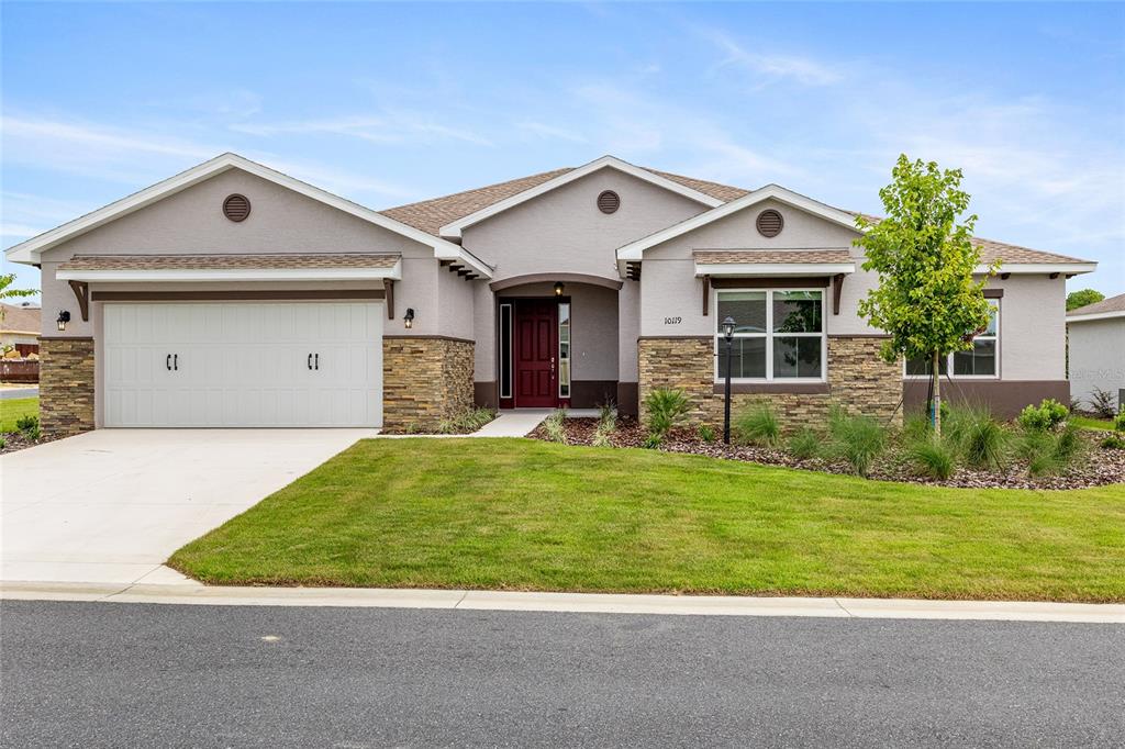 A single-story house with a white garage, stone accents, and a red front door — 10119 SW 106TH CIRCLE, OCALA, FL