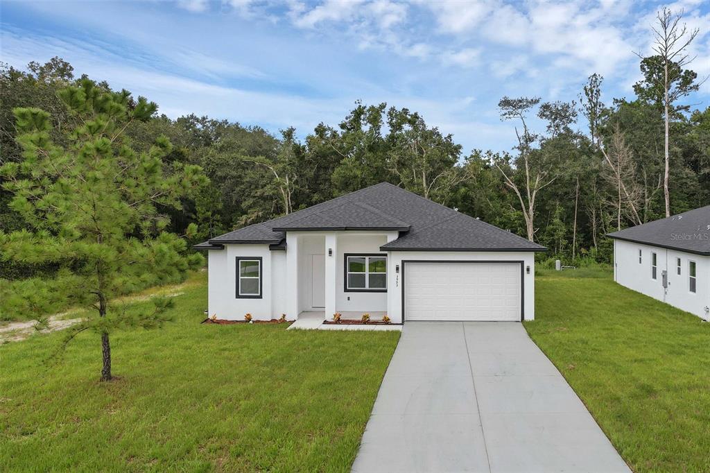 A white single-story house with a dark roof and a two-car garage sits on grass — 21723 SW BEACH BOULEVARD UNIT 1, DUNNELLON, FL