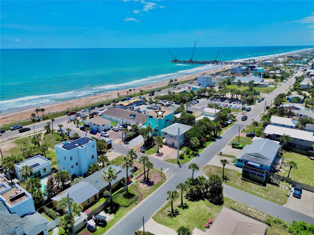 An aerial view shows a teal multi-story house near a beach with construction cranes offshore — 107 6TH STREET N, FLAGLER BEACH, FL
