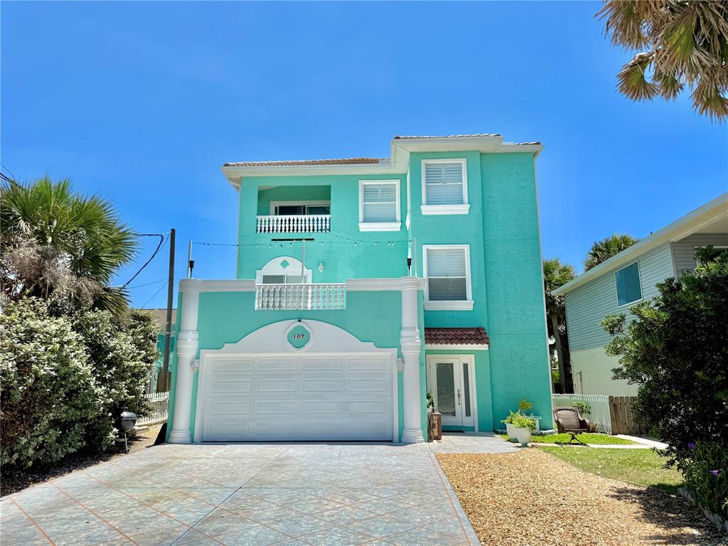A three-story teal house with a two-car garage and a paved driveway — 107 6TH STREET N, FLAGLER BEACH, FL
