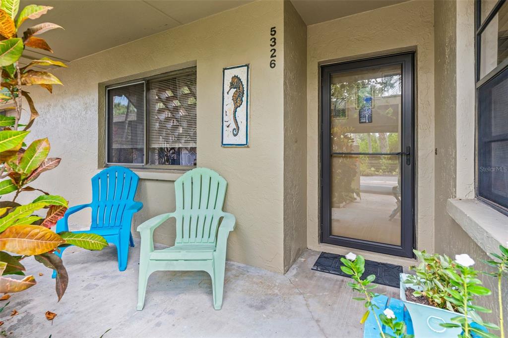 A front porch features two plastic chairs, a seahorse wall decoration, and a glass door — 5326 LAKE ARROWHEAD TRAIL UNIT 7, SARASOTA, FL