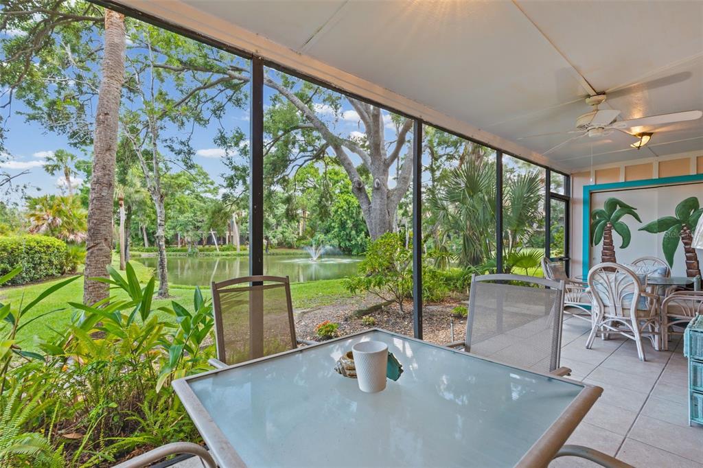 A screened-in patio features a glass-top table, tile flooring, and a view of a pond — 5326 LAKE ARROWHEAD TRAIL UNIT 7, SARASOTA, FL